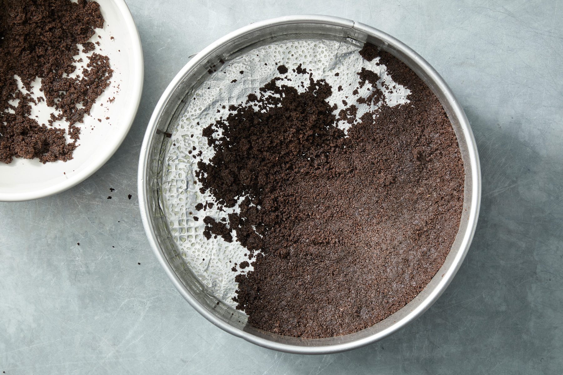 Overhead shot of press onto the bottom and 1 inch up the side of a greased 9-inch springform pan; all set on a grey surface;