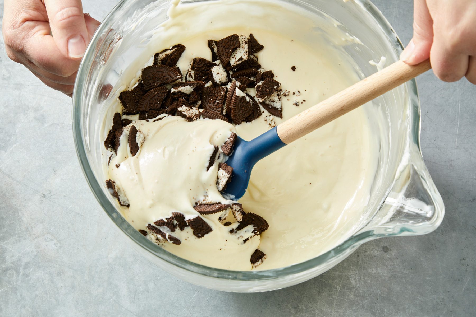 Overhead shot of a large glass jar with a spatula folding in 1-1/2 cups of chopped cookies; on a grey surface;