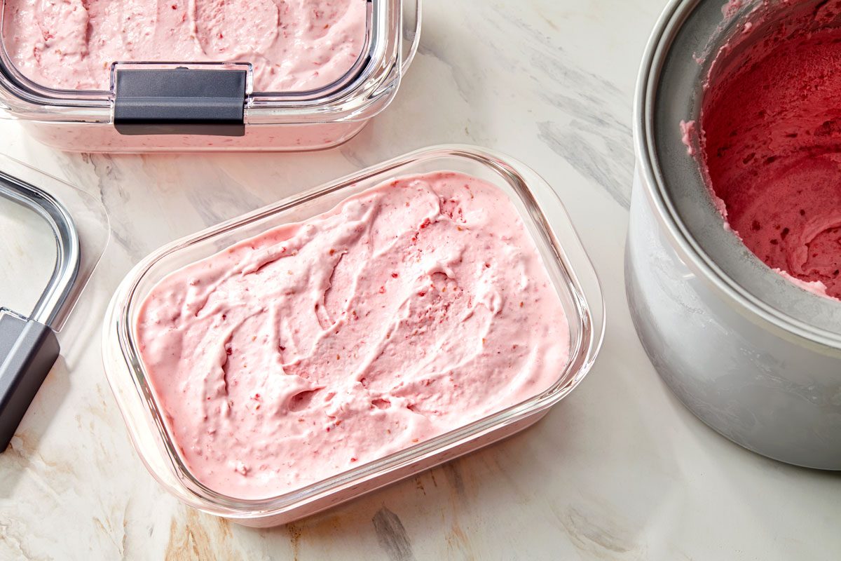 Scooping raspberry ice cream into freezer containers.