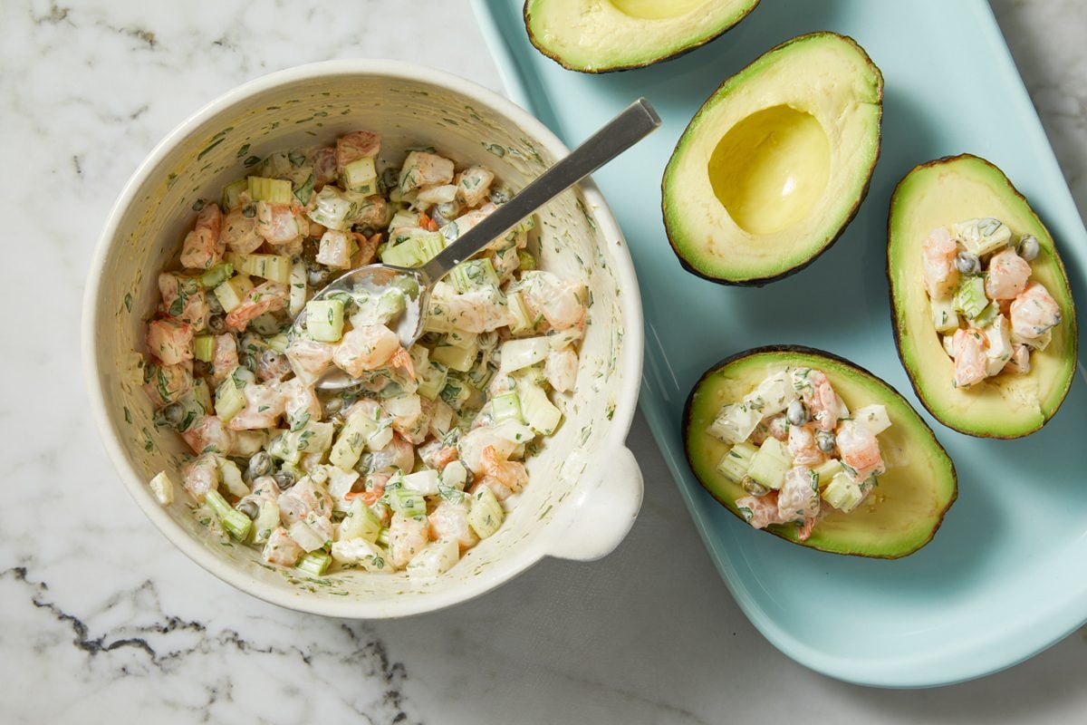 Overhead shot of spoon into avocado halves; marble surface;