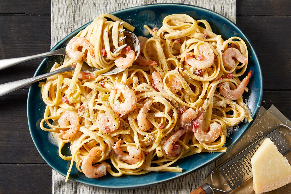 Overhead shot of Spicy Shrimp Fettuccine Alfredo; Garnished with grated parmesan cheese; served in a large bowl with forks and spoon