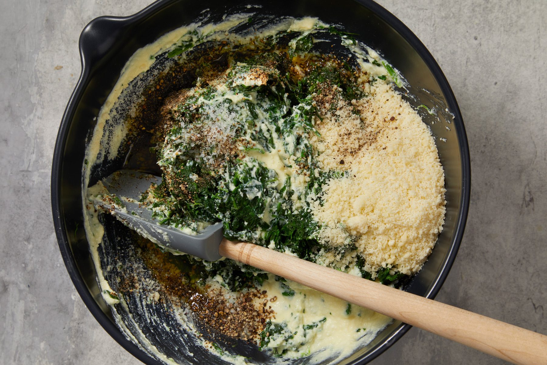 Overhead shot of stir in spinach; parmesan; oil; salt and pepper; spatula; marble surface;