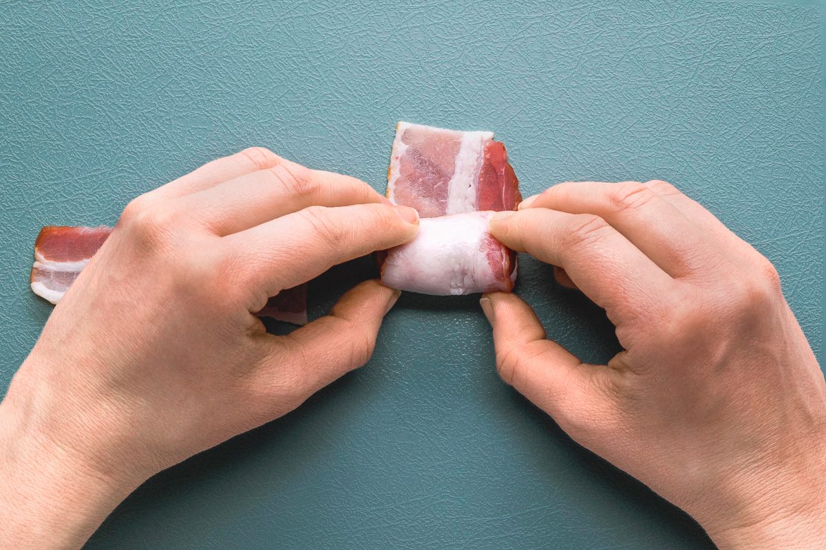 wrapping piece of bacon around sausage