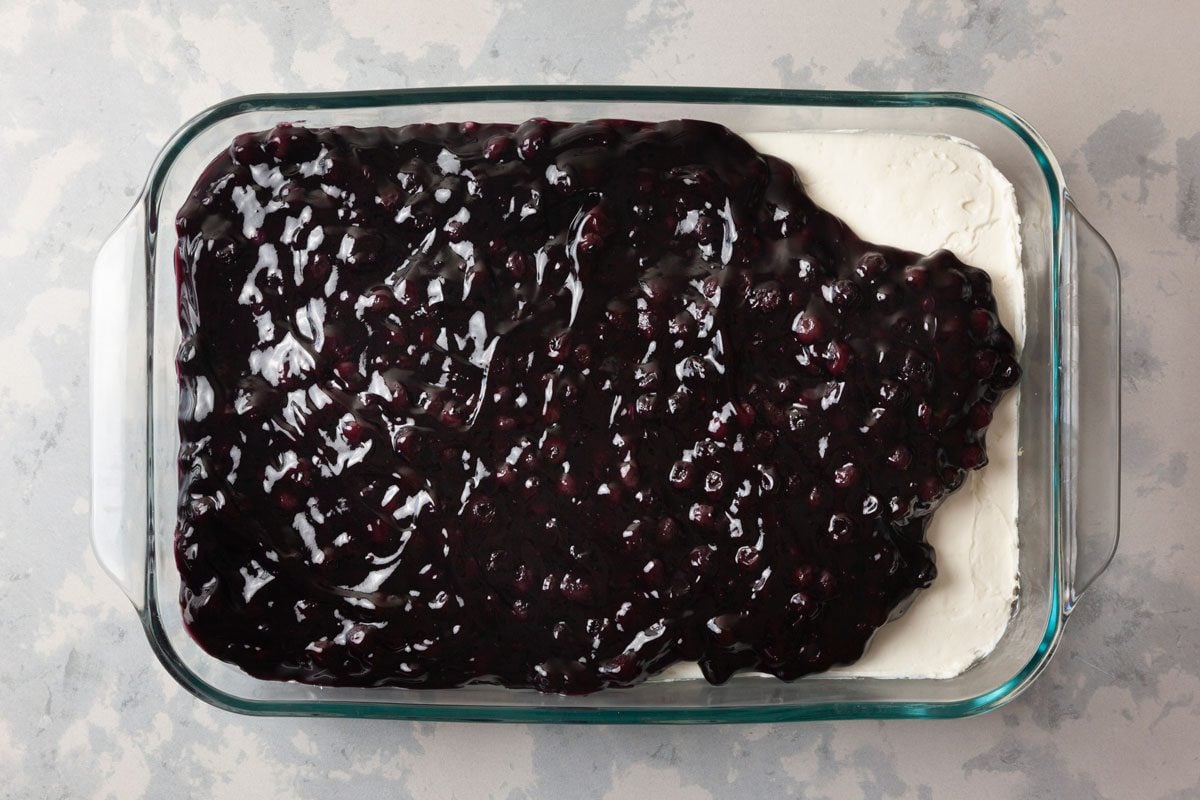 overhead shot of a glass baking dish filled with a dessert that has a creamy white layer at the bottom, topped with blueberry sauce; the dish sits on a light colored surface