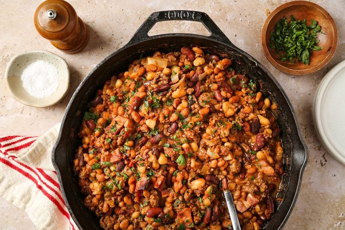 A cast iron skillet filled with a colorful mixed bean stew garnished with herbs.
