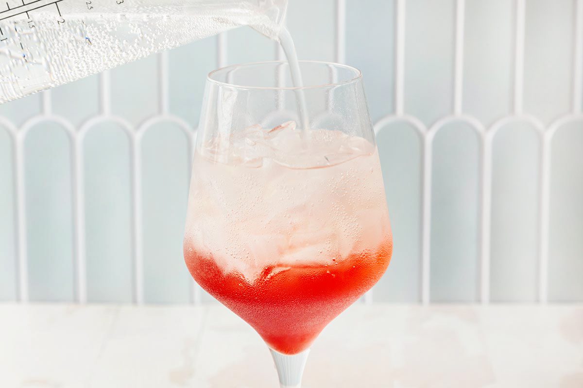 Club soda being poured into the wine glass filled with campari