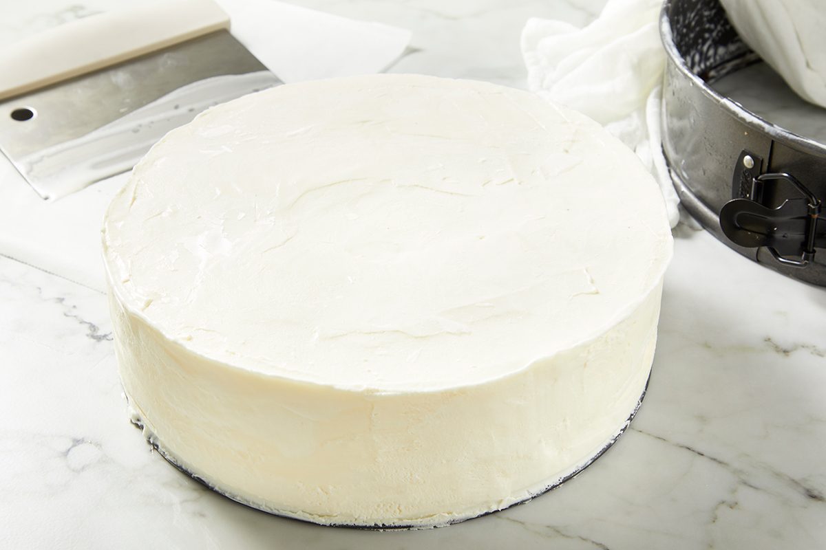 A round, unfrosted cake with a smooth white icing layer on a marble countertop. 