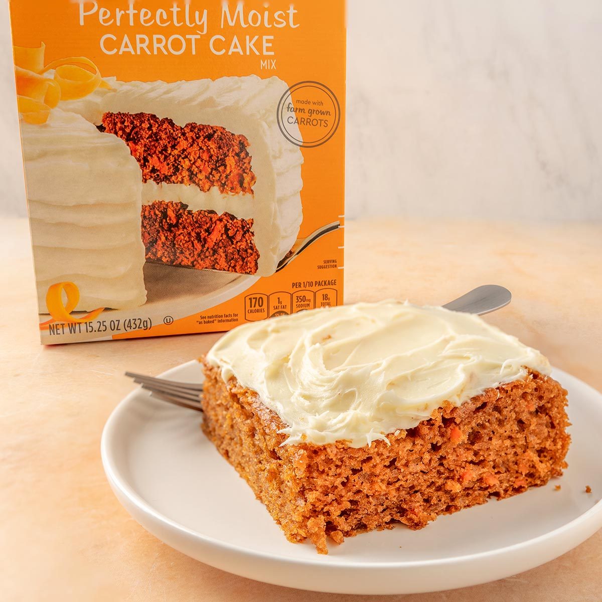 Duncan Hines slice of carrot cake with cream cheese frosting on a white plate with the box in the background