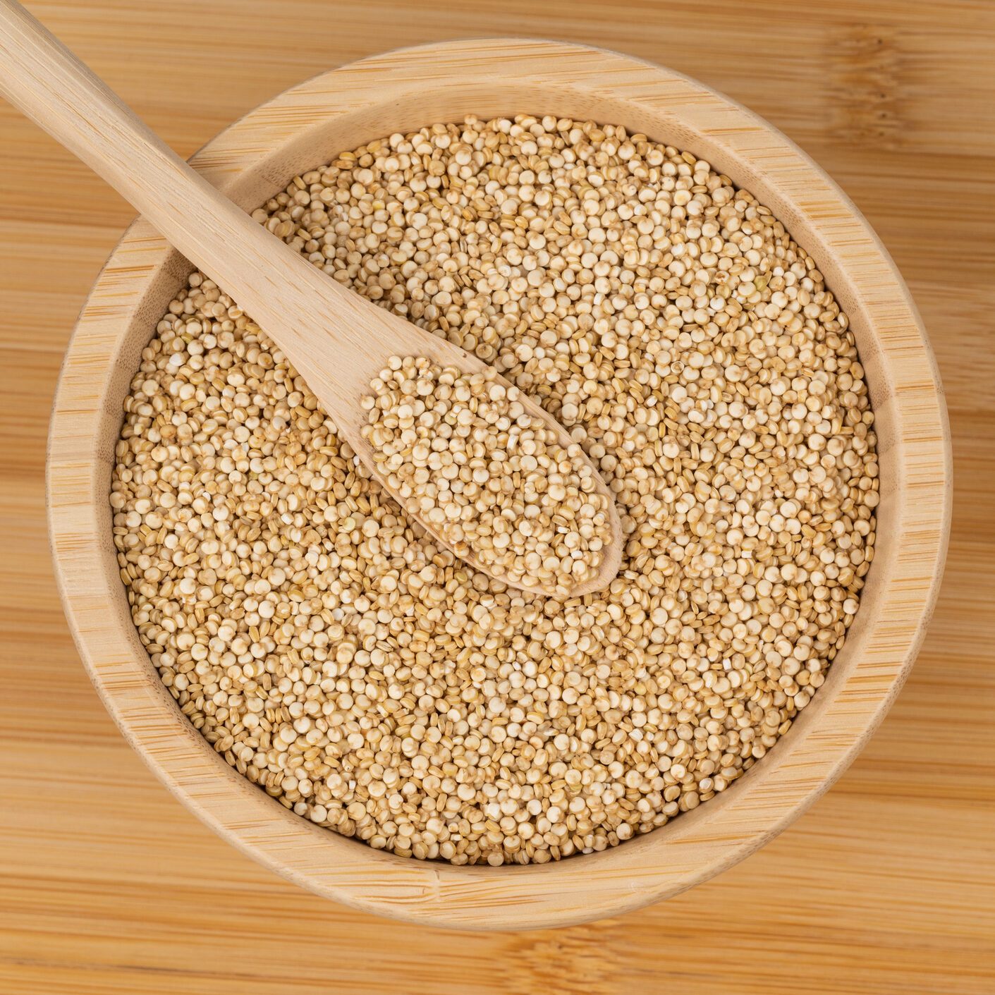 Quinoa seeds in a wooden bowl with a spoon on a bamboo surface