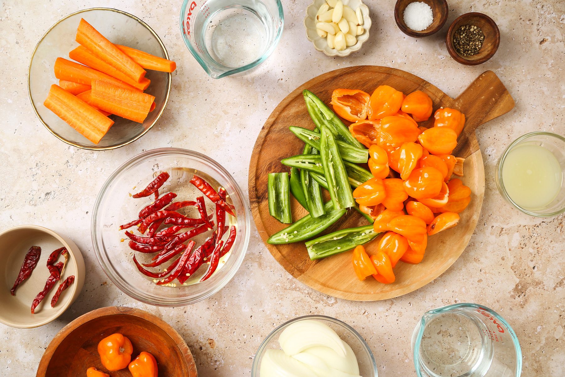 Overhead shot of cut habanero and serrano peppers in half; discard stems and seeds; wooden round board; a bowl; combine arbol chiles and enough boiling water to cover; Let stand; covered 10 minutes; drain; marble surface;