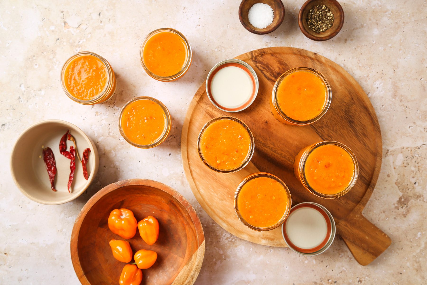 Overhead shot of Carefully ladle mixture into hot half-pint jars; leaving 1/2-inch headspace; Remove air bubbles and adjust headspace if necessary by adding hot mixture; Wipe rims; Center lids on jars; screw on bands until fingertip tight; round wooden board; marble surface;