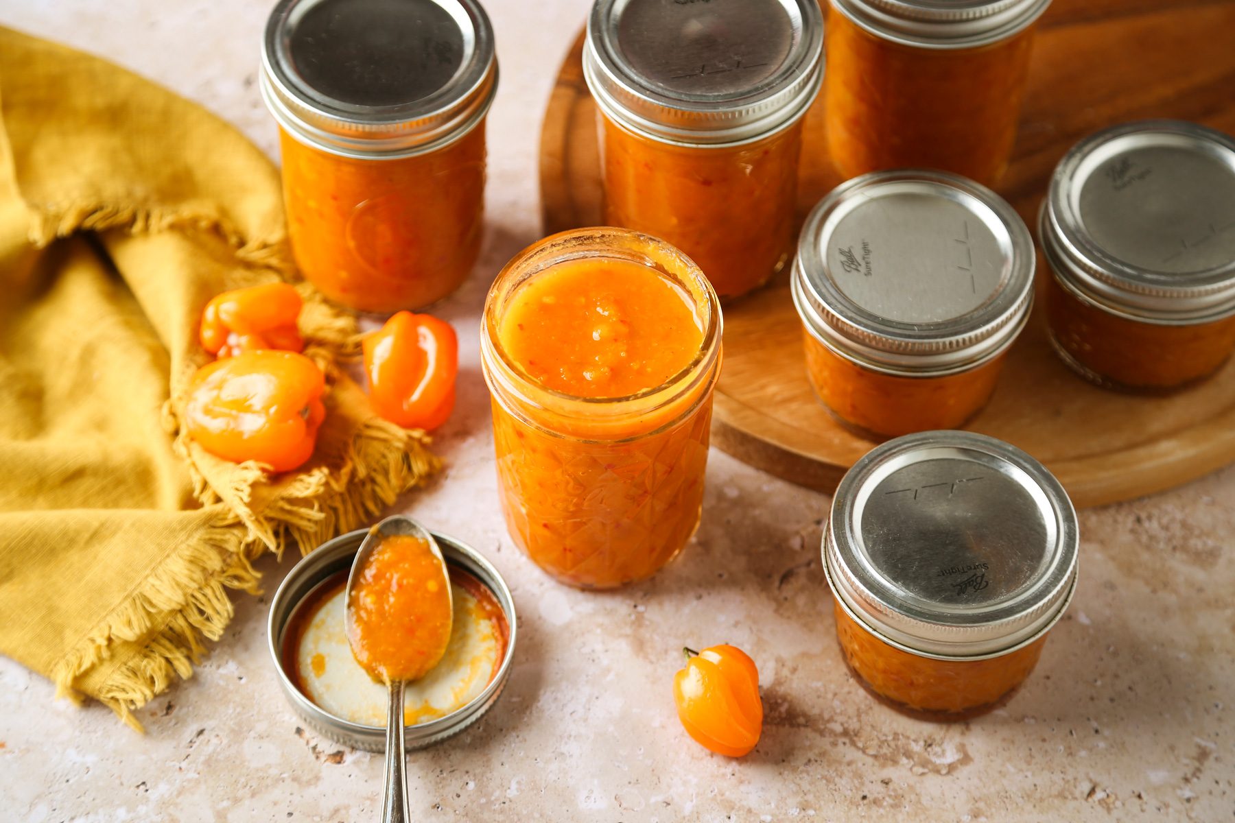 High angle view shot of Homemade Spicy Hot Sauce; stored in jars; round wooden board; yellow napkin; marble surface;