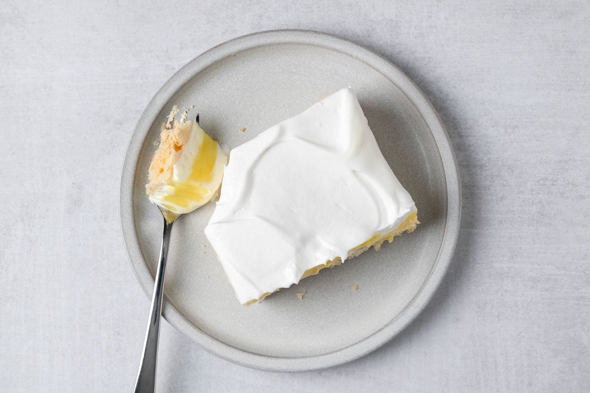 overhead shot of a slice of Lemon Lush presented on a pale, round plate; on which a fork rests