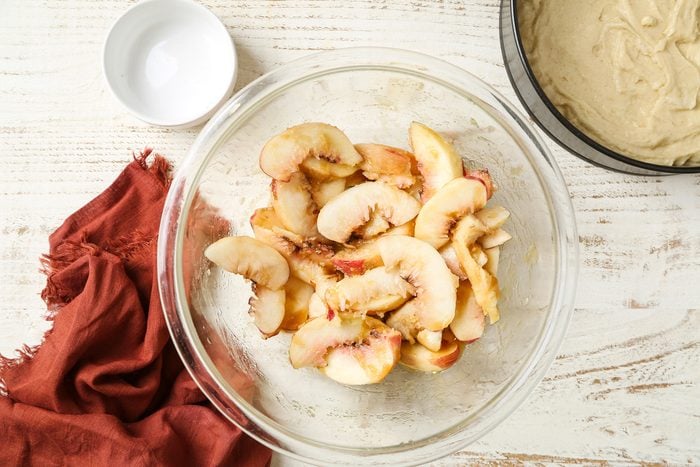 Overhead shot; a large bowl, stir together brown sugar and butter to form a wet paste; Stir in peaches; Spoon peach mixture evenly over top of cake batter; Bake until a toothpick inserted in the center comes out clean 40-45 minutes; napkin; white wooden surface;