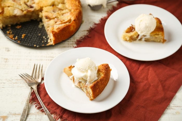 Table view shot of Warm Peach Cake; served warm on two white plates with vanilla ice cream; forks; napkin; white wooden surface;