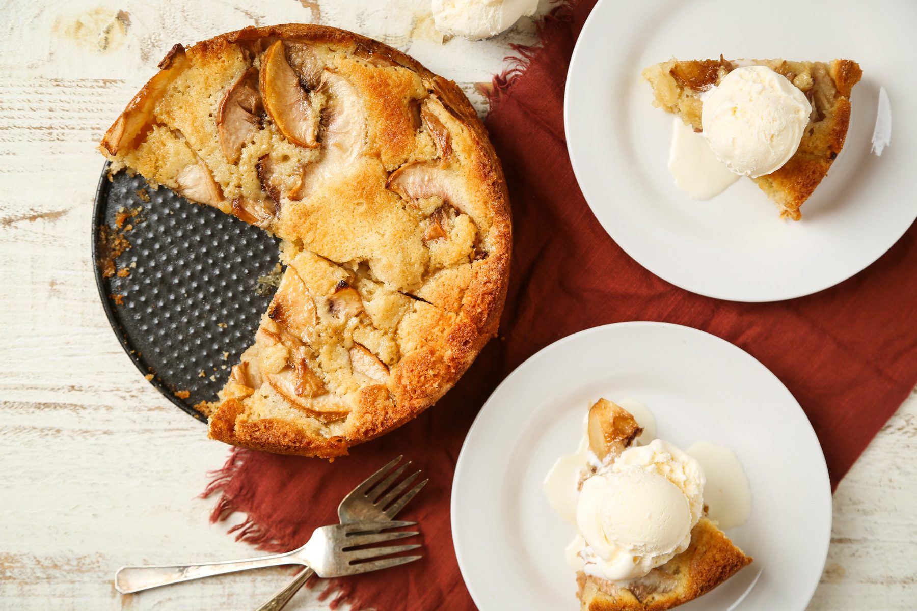Top view shot of Warm Peach Cake; served warm on two white plates with vanilla ice cream; forks; napkin; white wooden surface;