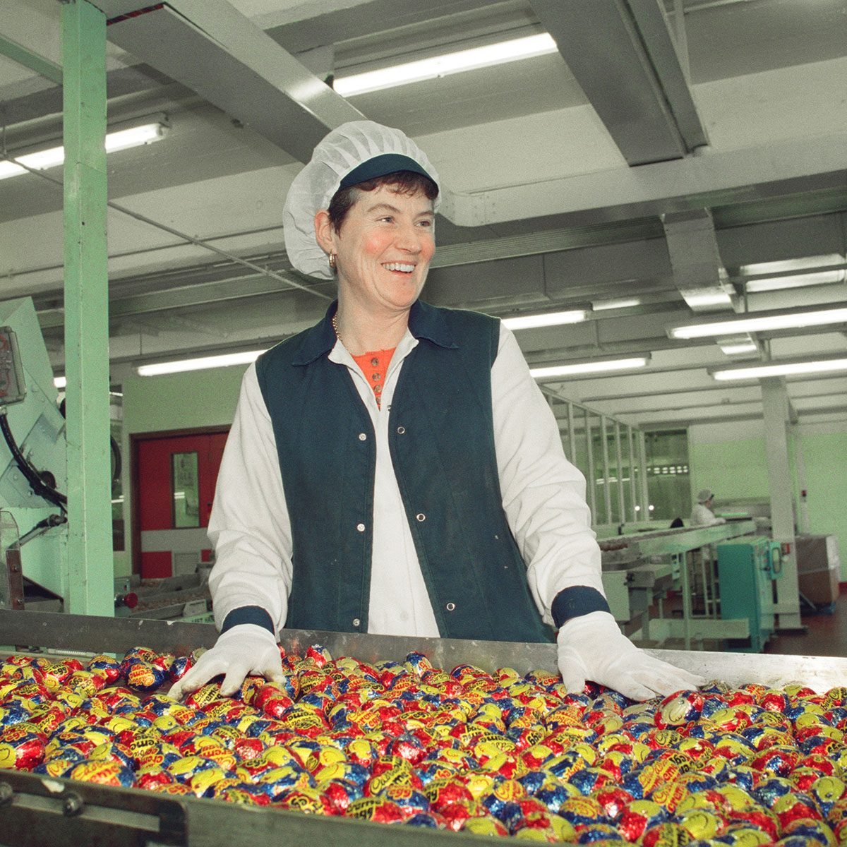 Worker stands behind a conveyor belt of cadbury creme eggs in a factory