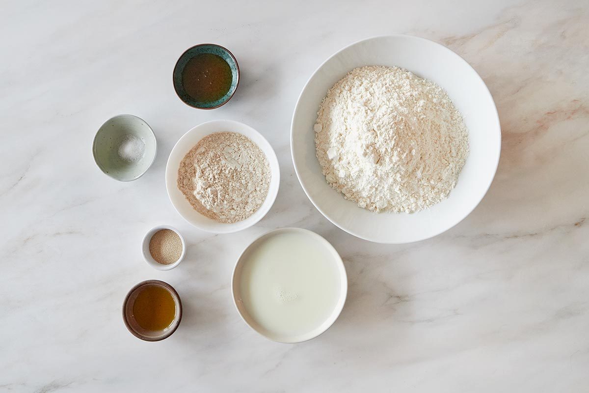 Several bowls of flour and other bread ingredients on a white stone countertop