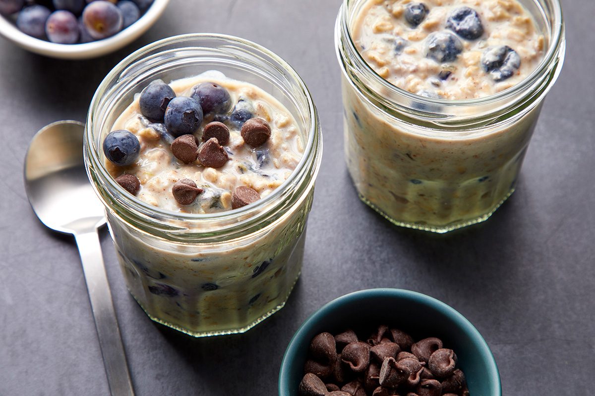Overhead shot of Blueberry Overnight Oats in two glass jars; served with chocolate chips; granola; and additional berries on top