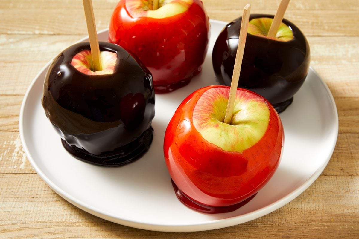 Close-up shot of Black-Hearted Candy Apples; placed on a large plate; all set on a light brown surface;