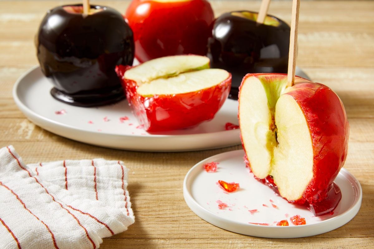 Table view shot of Black-Hearted Candy Apples; placed on a large plate in background; and a half cut red-hearted candy apple on a samll plate at front; a napkin; all set on a light brown surface;