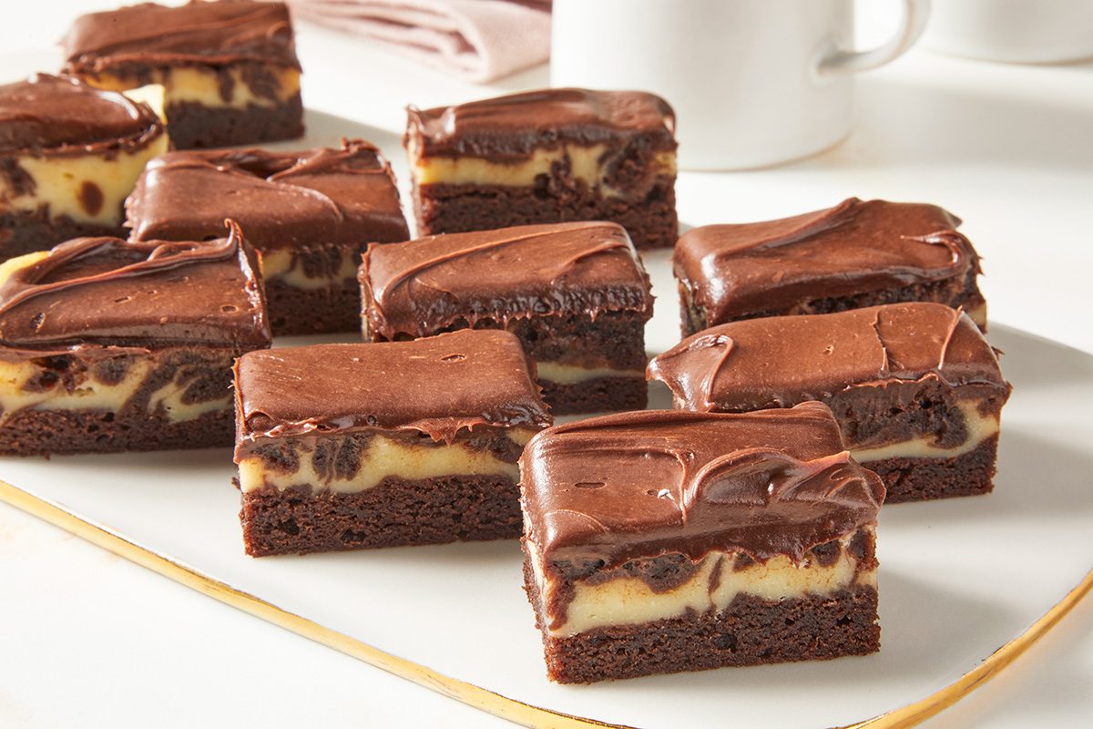 Close view shot of Cheesecake Brownie Squares; cut into squares and served them on a white serving tray; all set on a marble surface