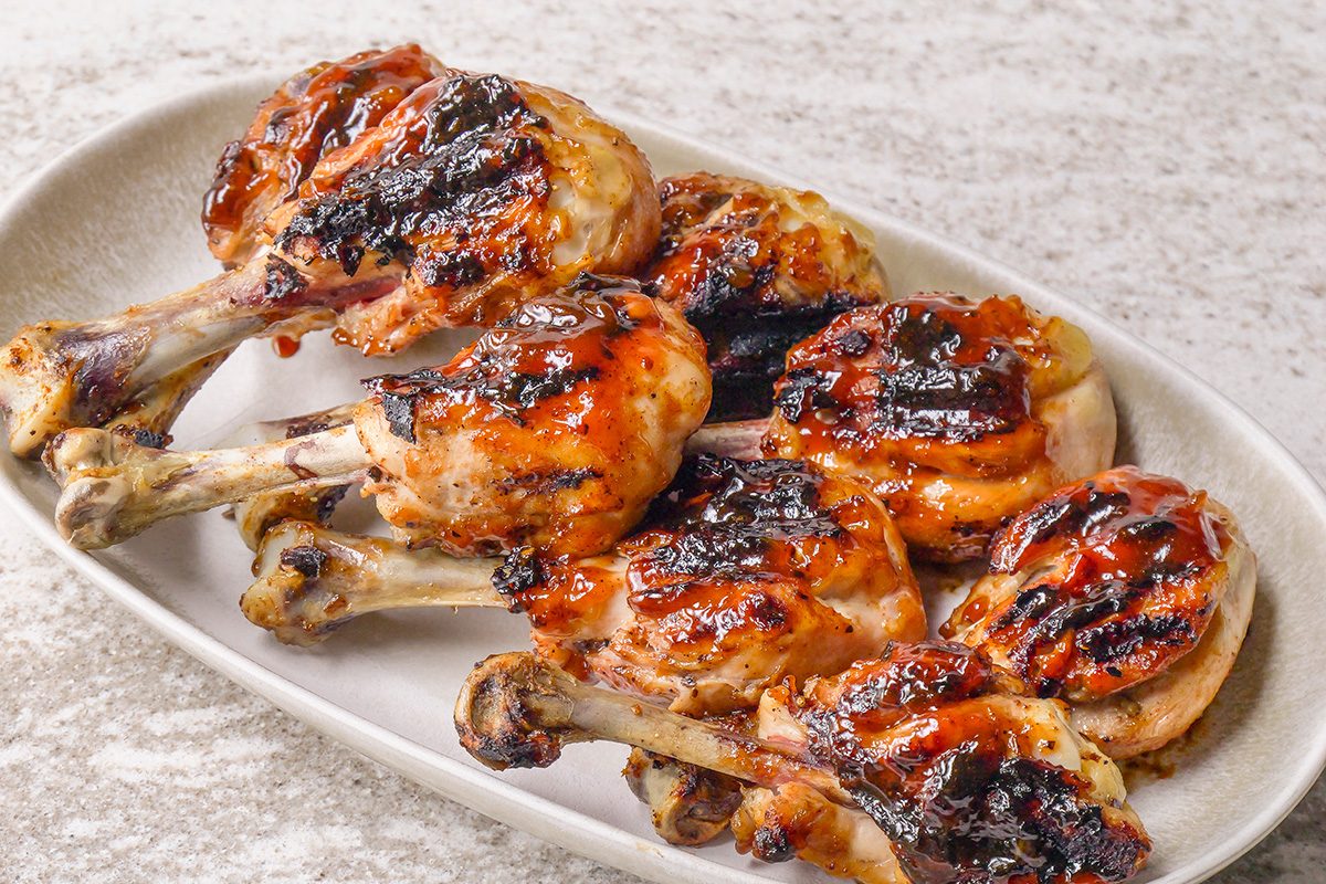 A plate of grilled chicken drumsticks glazed with barbecue sauce, showing charred grill marks and a glossy finish, arranged neatly on an oval dish.