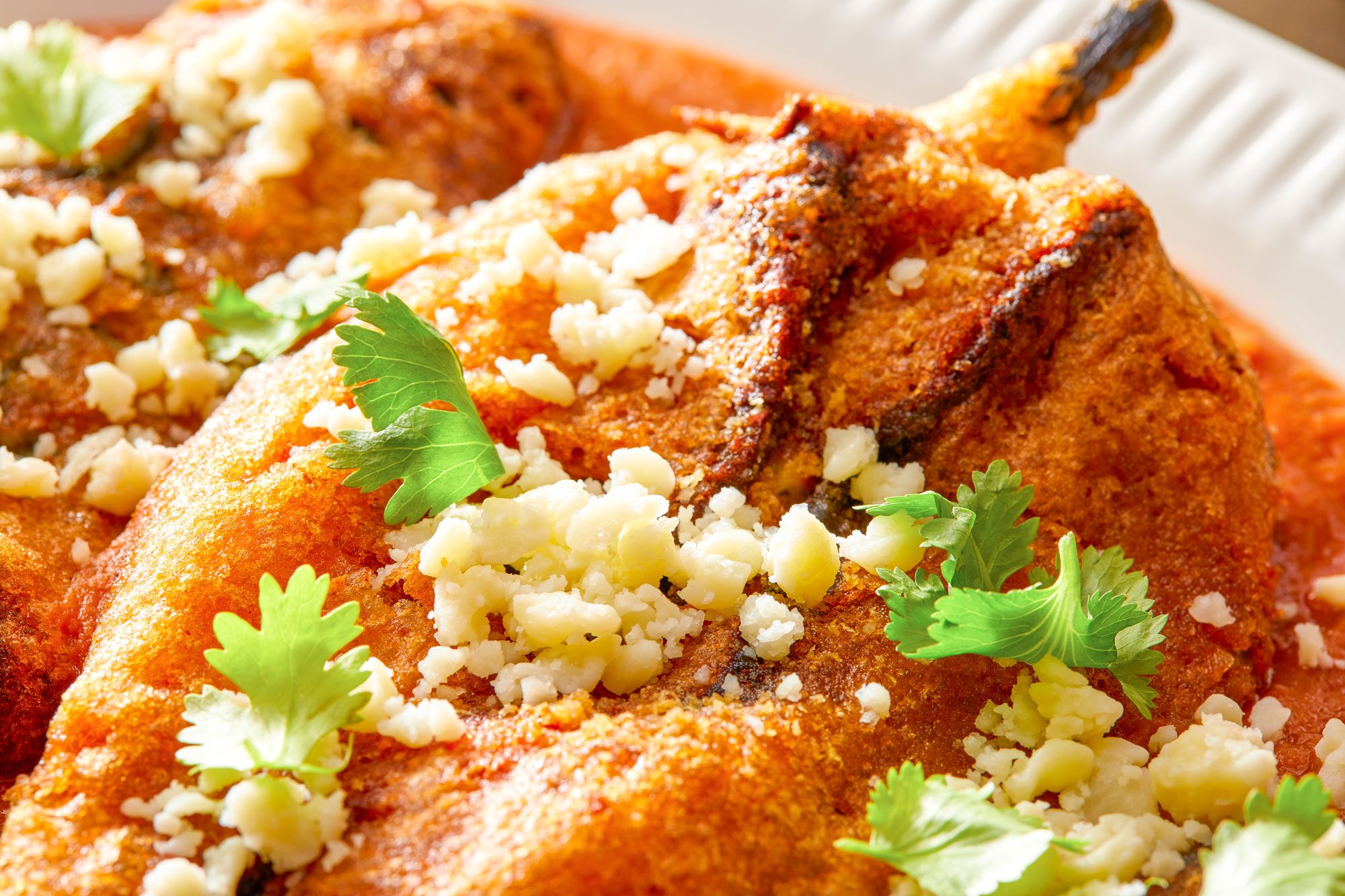 Close-up shot of Chile Rellenos; To serve spoon red sauce in shallow bowls; top with fried peppers; Sprinkle with cilantro and Cotija cheese; Serve immediately