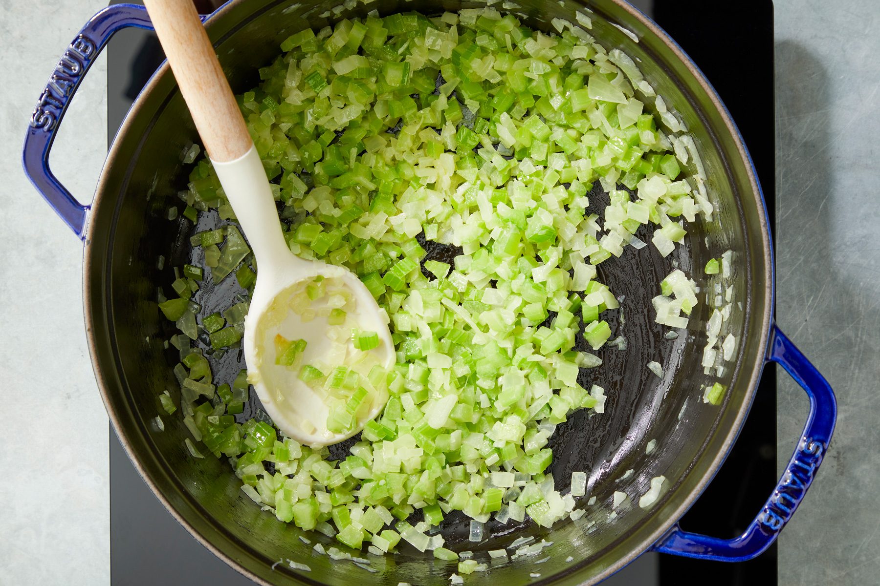 Overhead shot of a large saucepan; melt butter over medium heat; add onion and celery cook until tender 4-5 minutes; spoon; induction; grey surface;