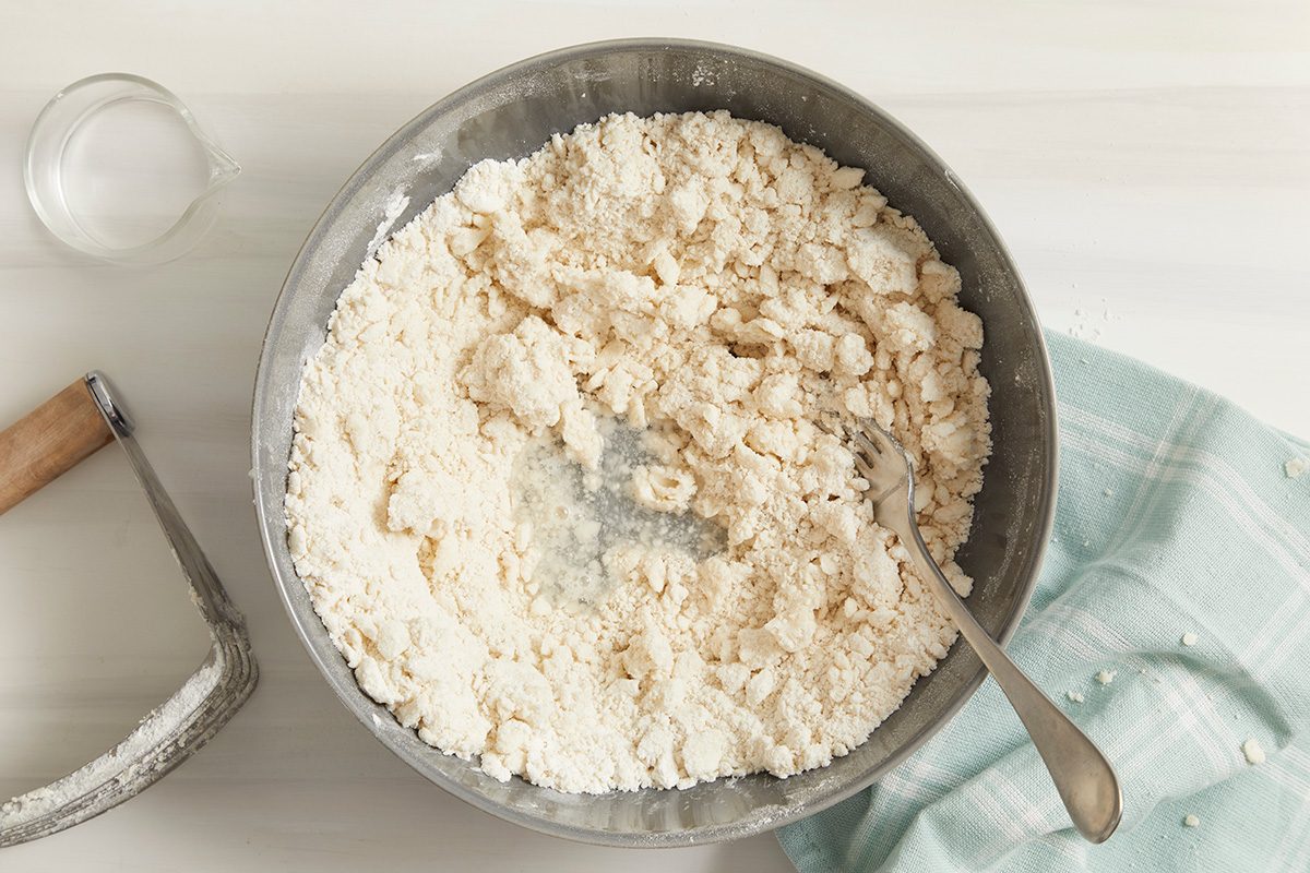 Overhead shot of gradually add cold water: a fork: a napkin: on cream surface
