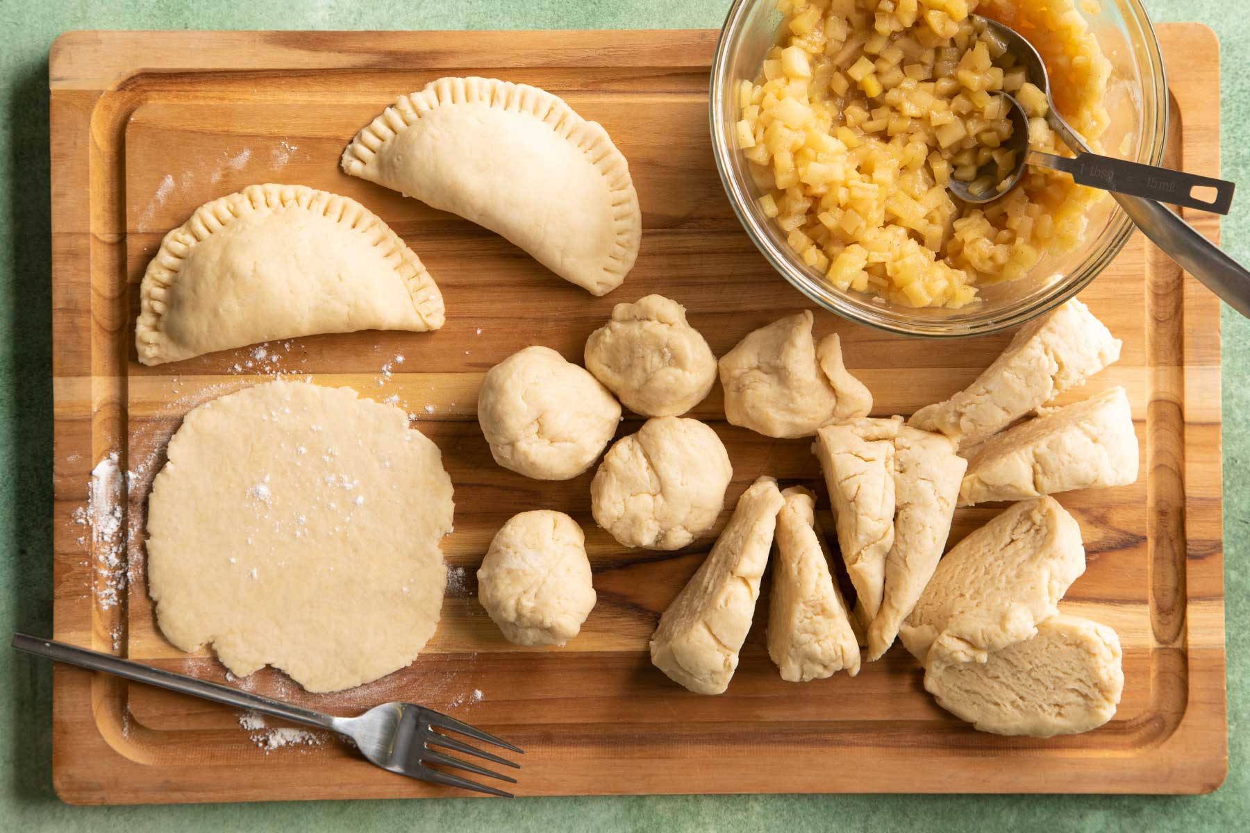 Overhead shot of preparing fried apple pies with filling kept on top of a wooden chopping board on a green marble countertop.