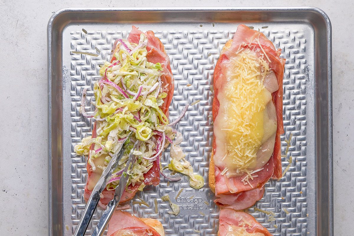 Grinder Sandwich, meat slices topped with some cheese, adding fresh veggies on the toast in eight pieces on a tray 