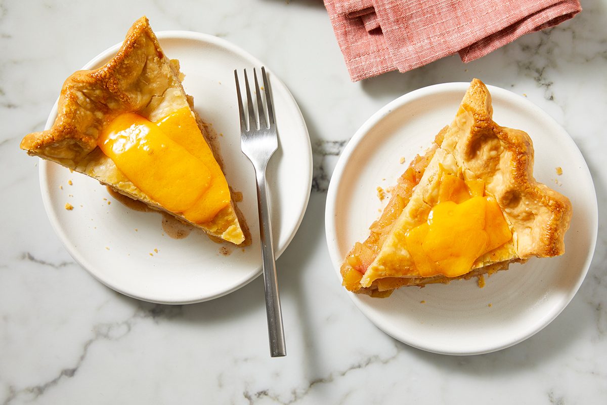 Two slices of pie topped with melted cheddar cheese are served on white plates with a fork on one plate, placed on a marble surface next to a folded pink napkin.