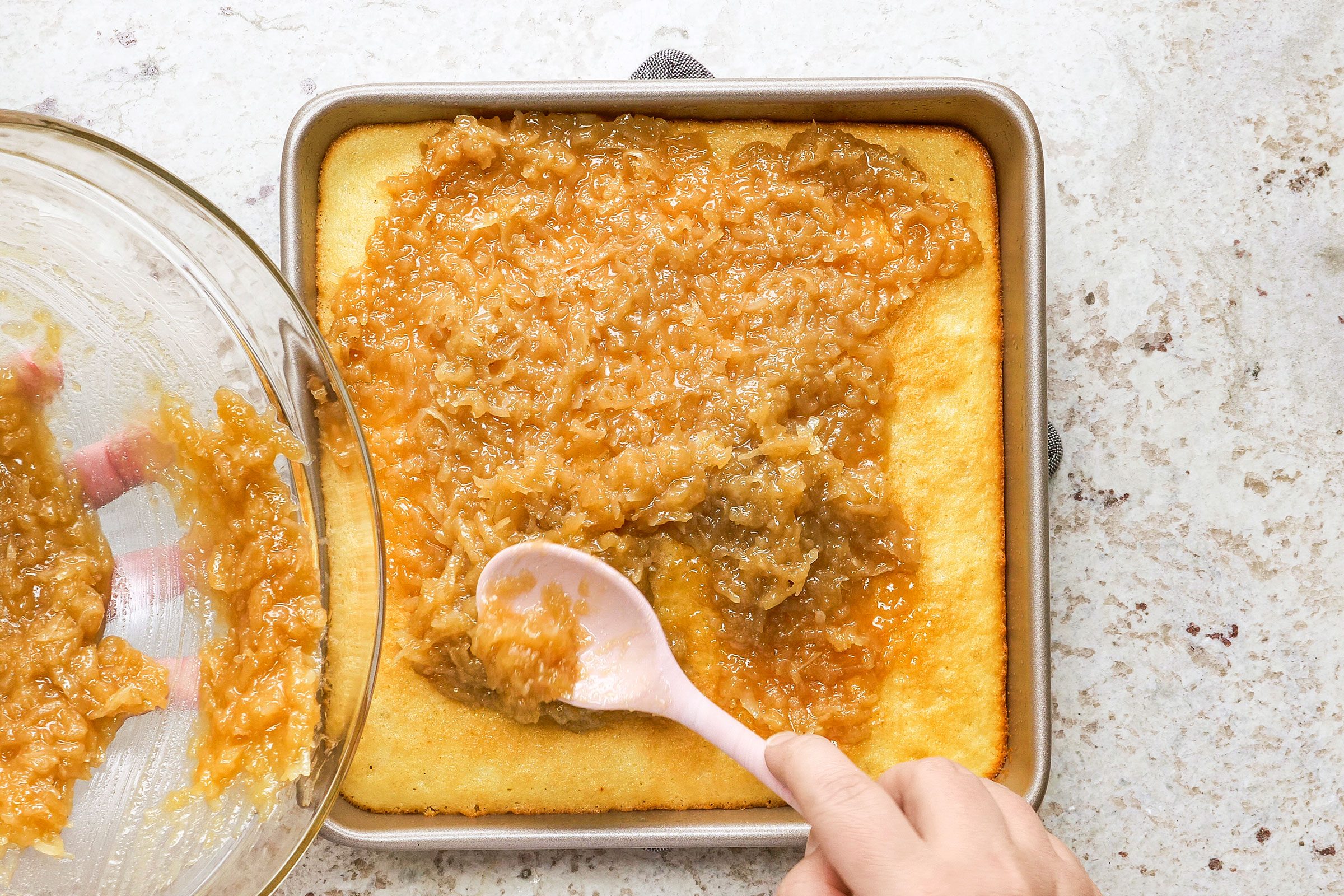 Spreading the sugar and coconut mixture over warm cake in a greased 9-inch square baking pan.