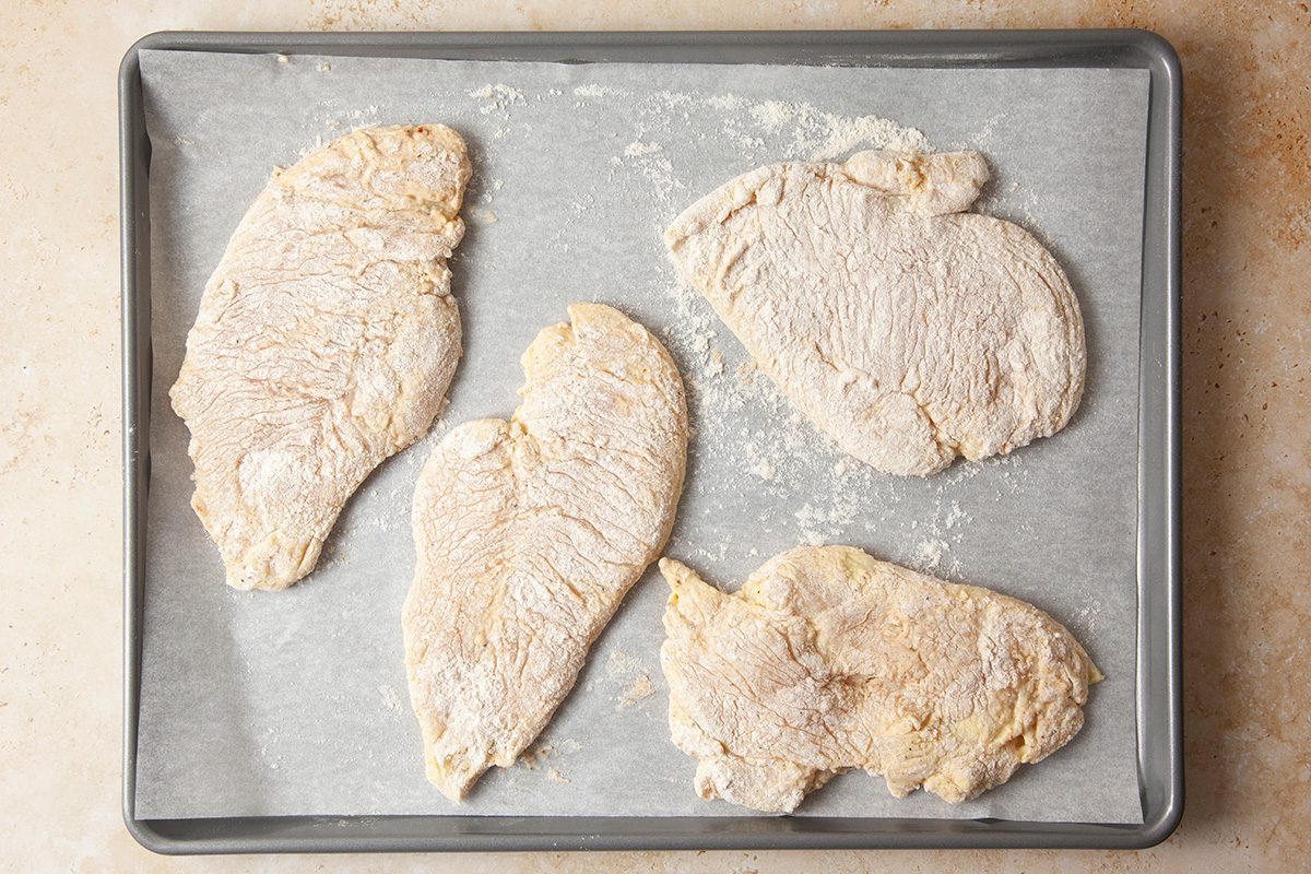 Four raw, breaded chicken cutlets are arranged on a parchment-lined baking sheet, ready to be cooked.
