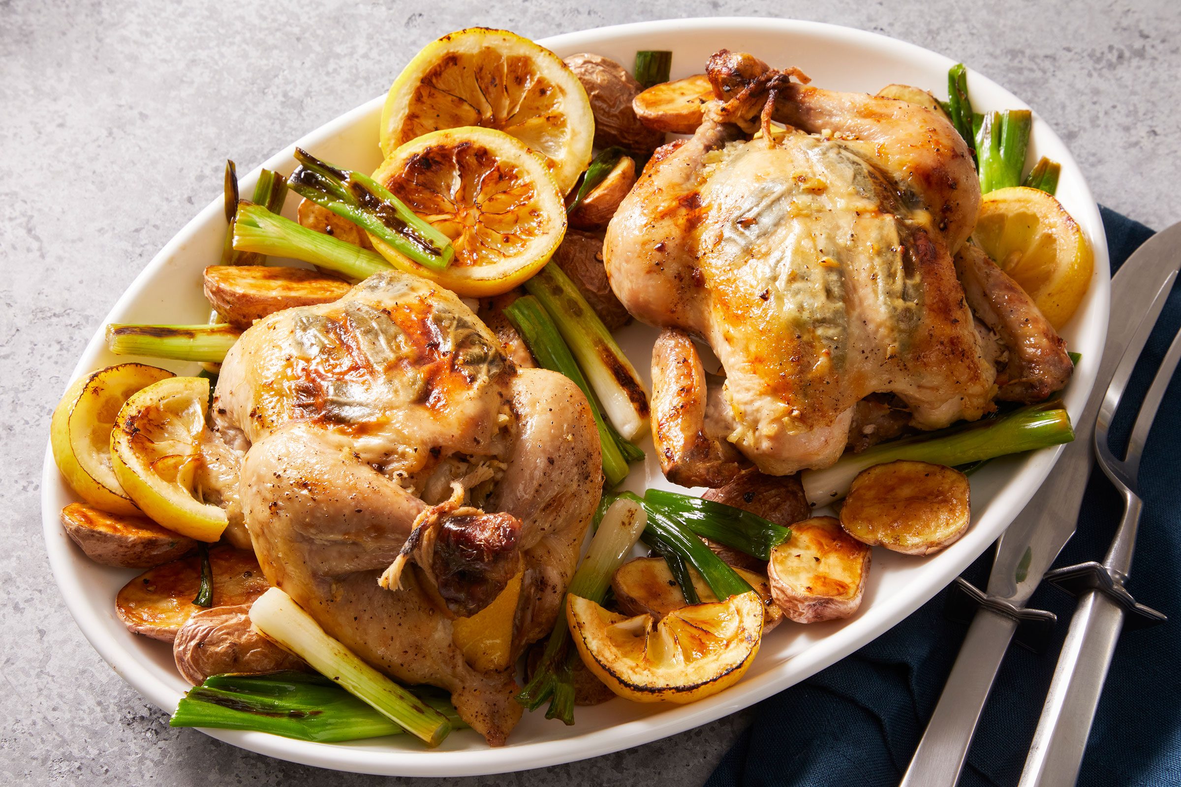 Roasted Cornish Game Hen served on a white plate with some vegetables and silverware kept on side