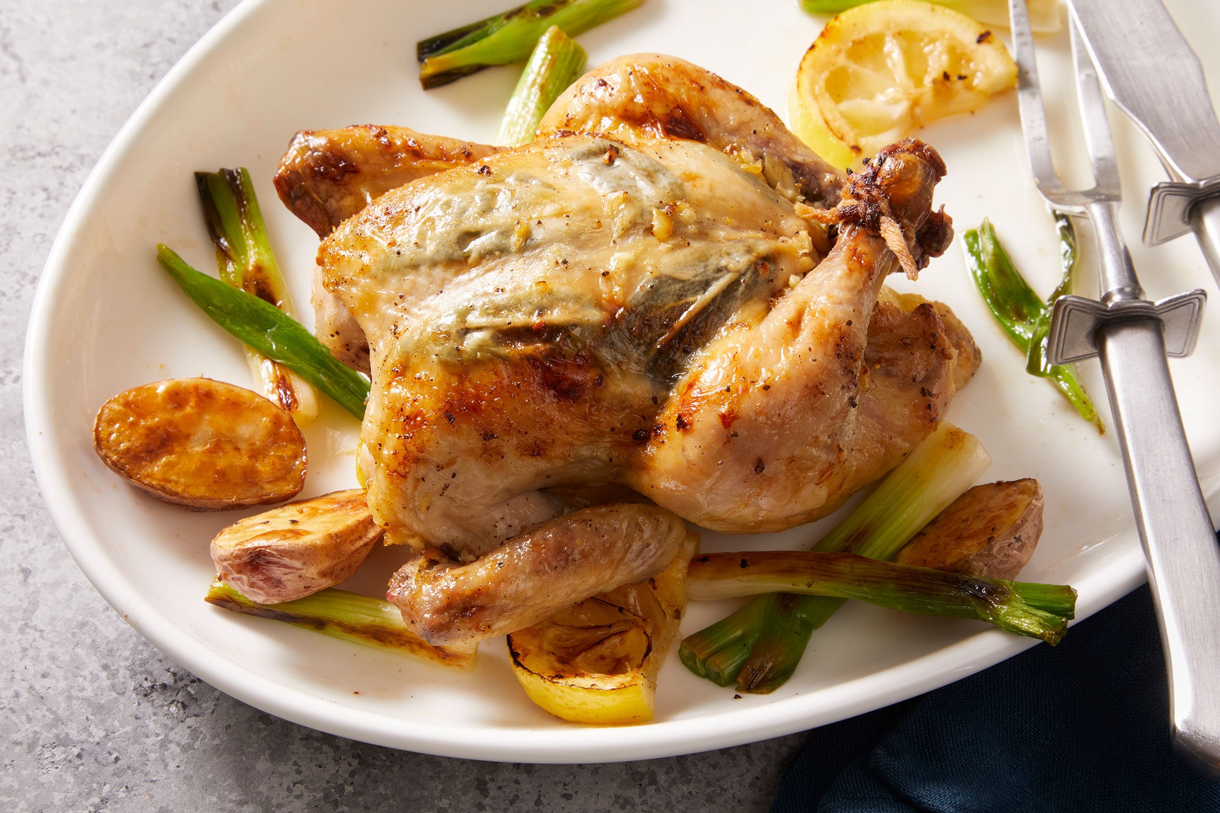 Roasted Cornish Game Hen served on a white plate with silverware kept on side