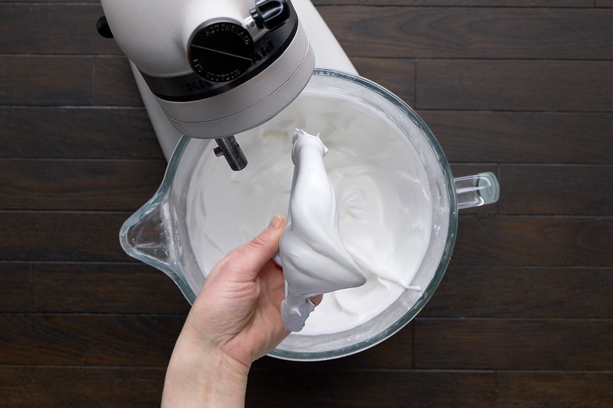 overhead shot of a hand is holding a mixing attachment coated with fluffy, white mix