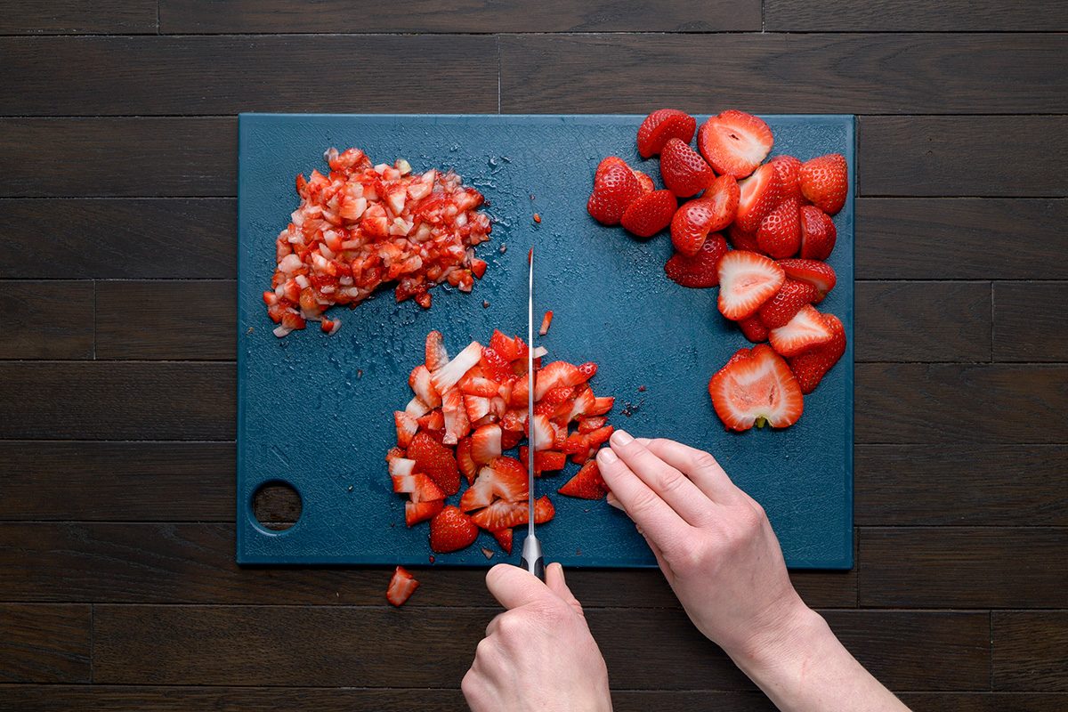 overhead shot of a chopped strawberries ;dark blue rectangular cutting board