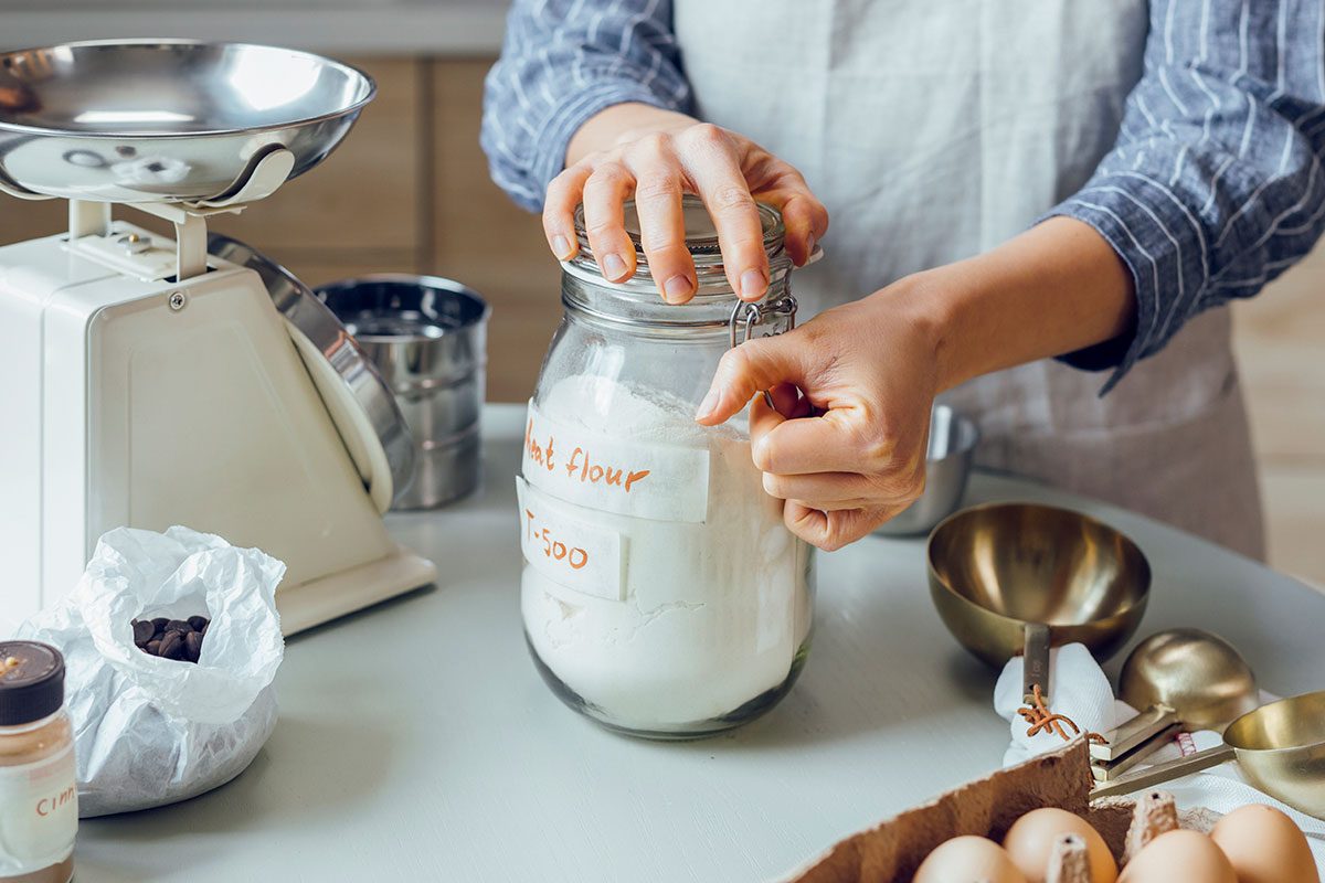 Woman in an Apron Opening a Jar of Flour to Make Cookies