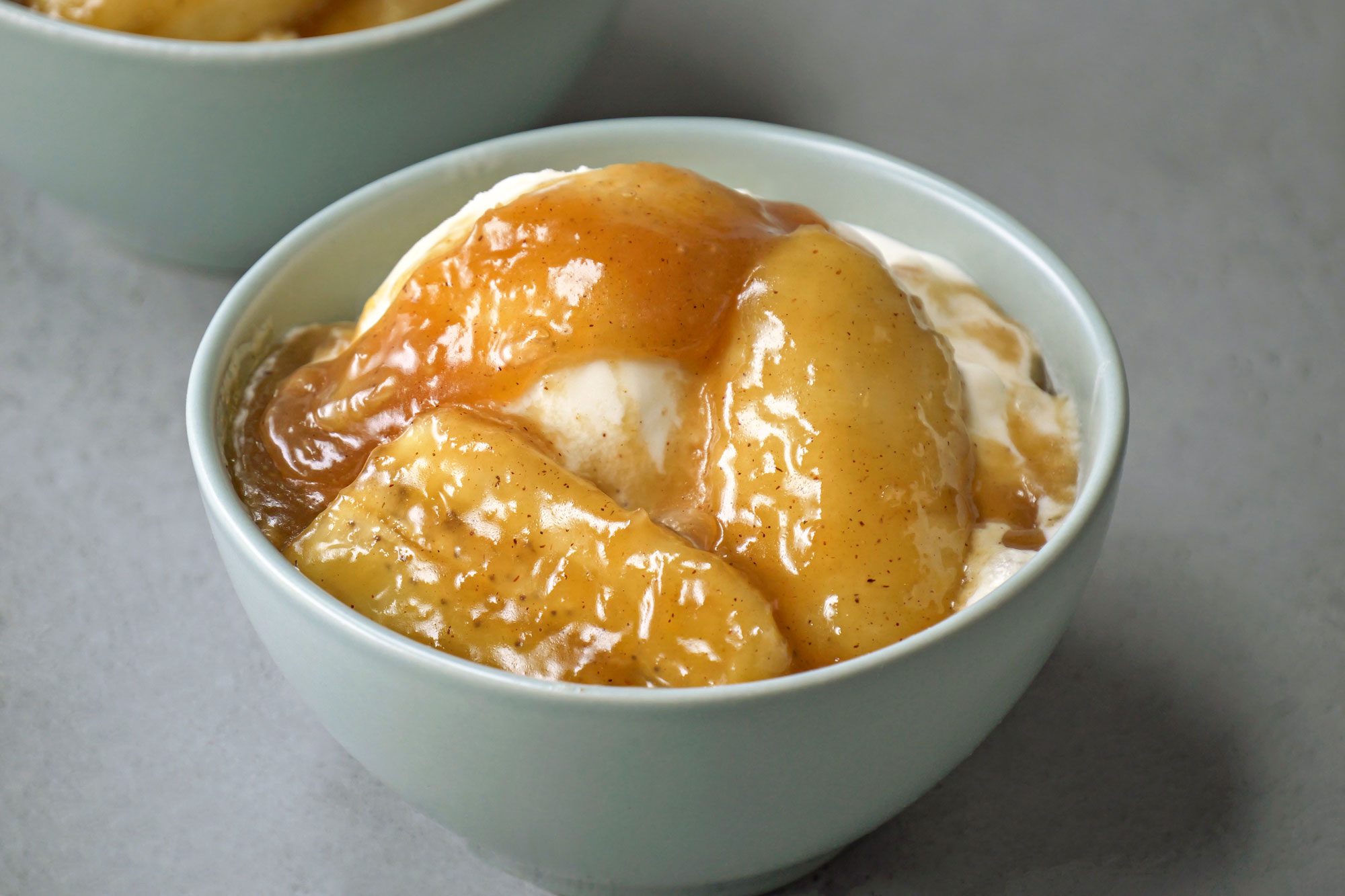 Overhead shot of Bananas Foster Sauce; Served warm with waffles, pancakes or vanilla ice cream as desired; two bowls; all set on a grey surface