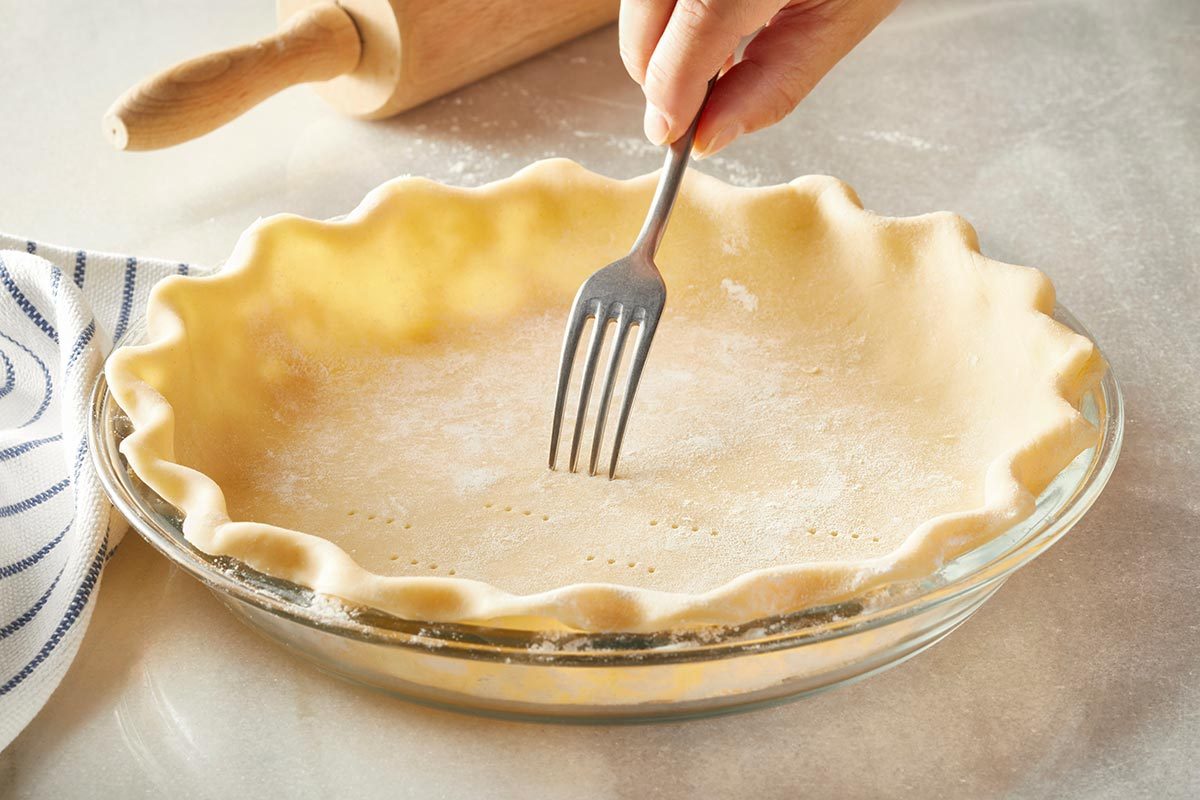 A fork is being pressed to the pie crust