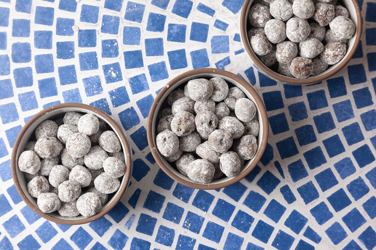 Three small bowls filled with round, powdered sugar-coated treats are arranged on a blue and white mosaic tile surface.