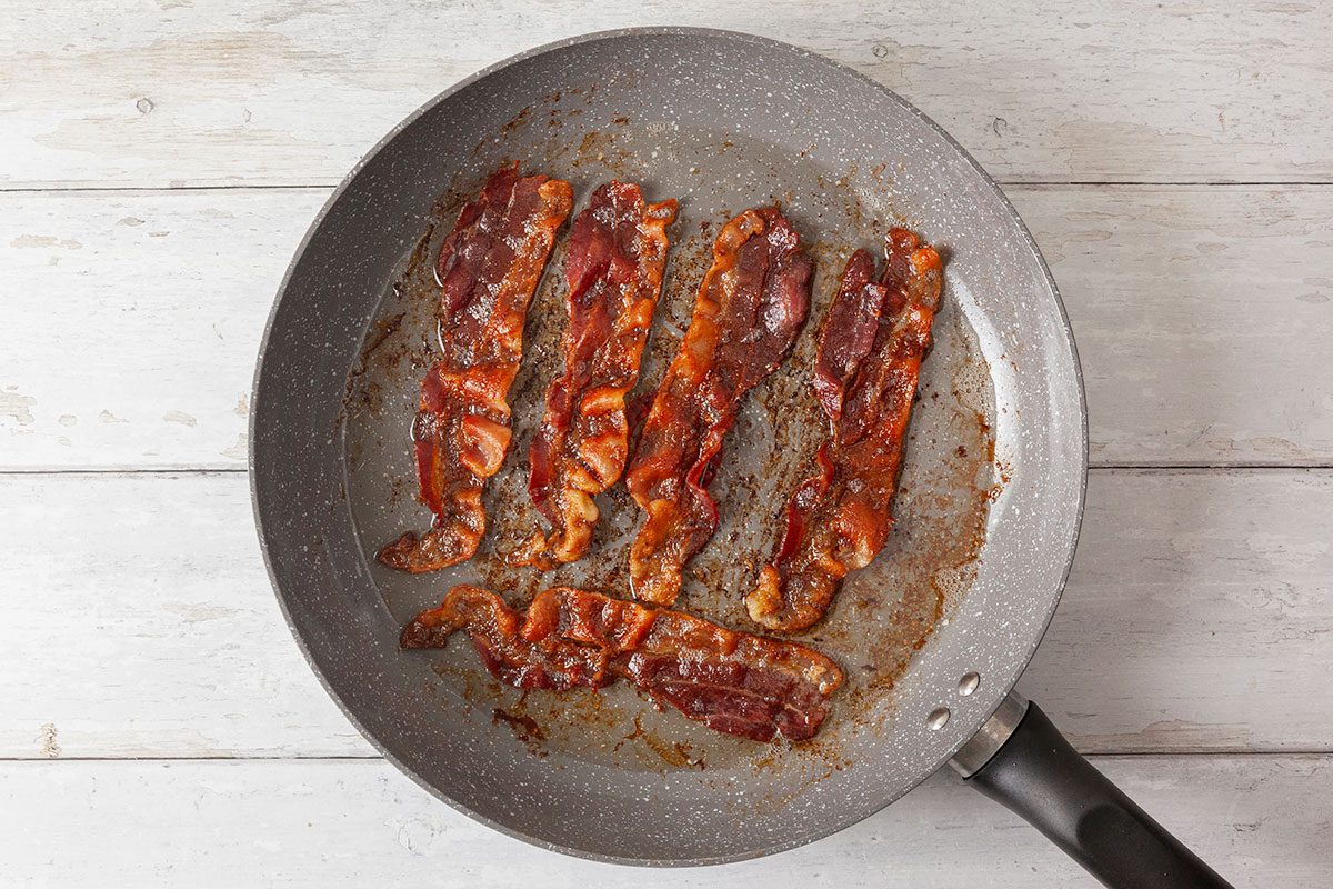 Bacon strips being cooked in large skillet pan
