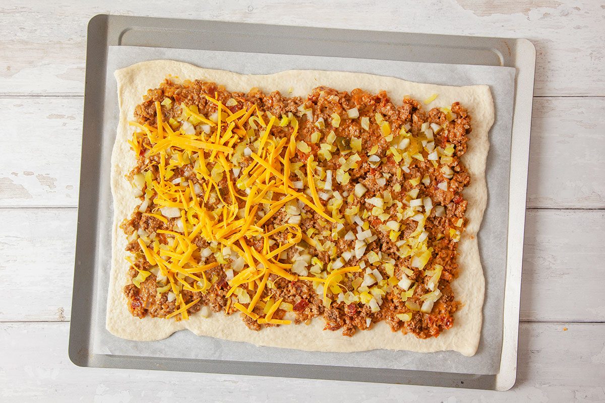 onion, banana and meat being added to the top of pizza dough