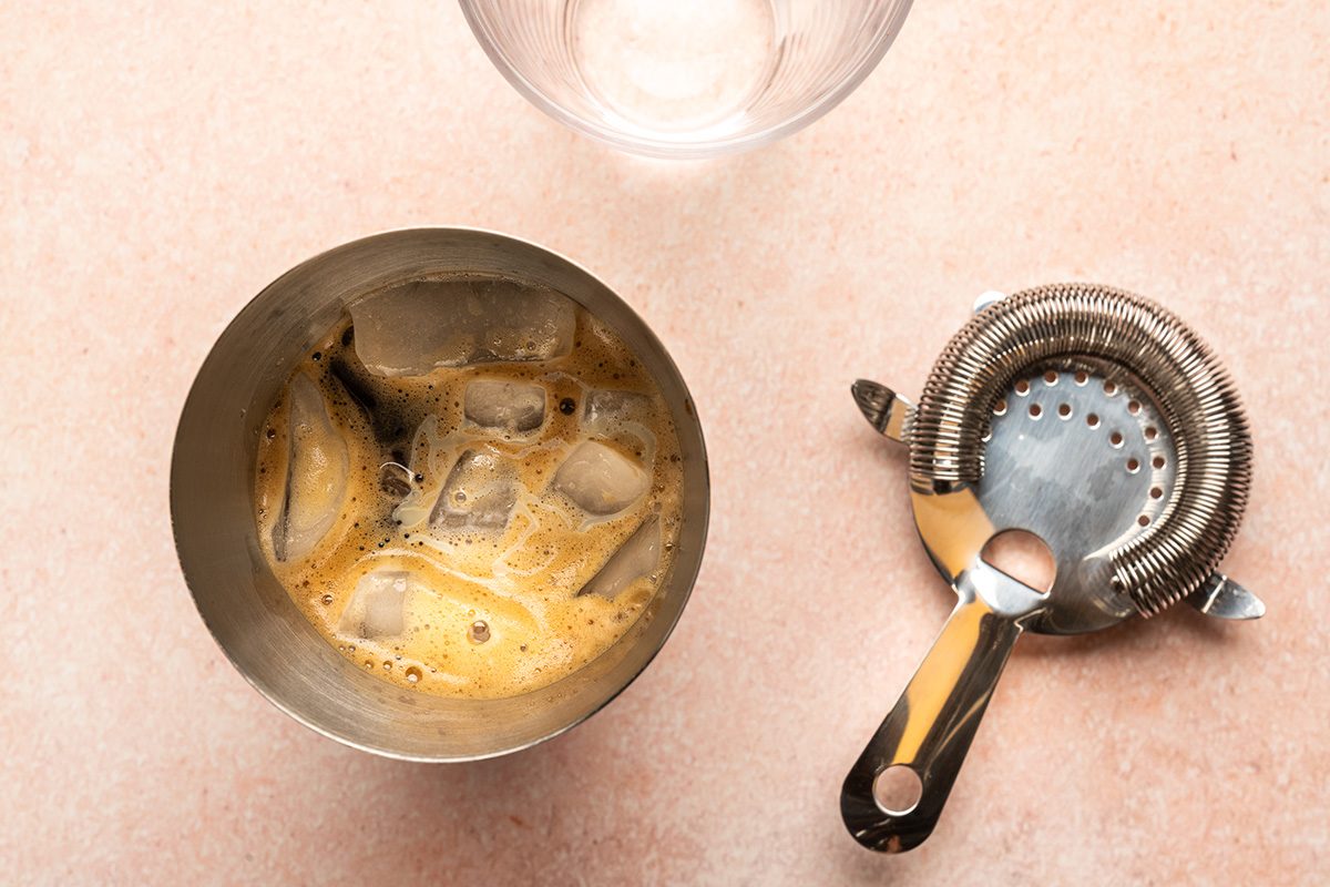 Glass with ice and espresso along with shaker and empty glass
