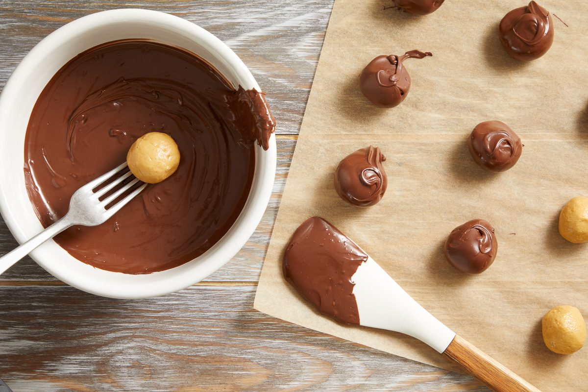 peanut butter balls being dipped in melted chocolate