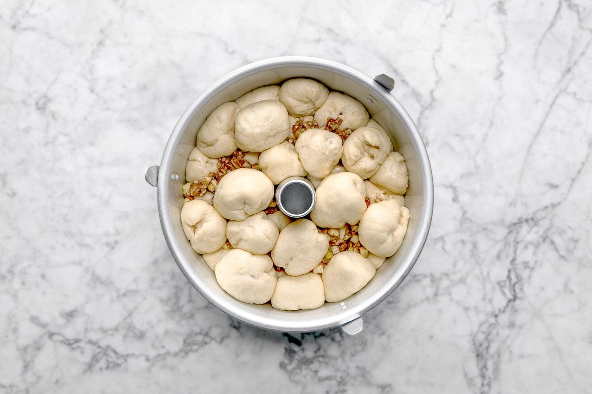 overhead shot of a bundt pan filled with unbaked dough balls, some nuts visible between the dough pieces, sits on a white marble surface
