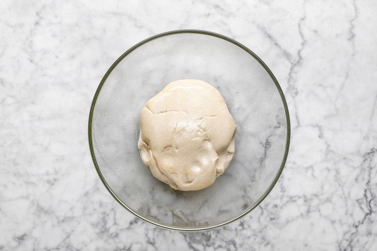 overhead shot of a ball of dough rests in a clear glass bowl on a white marble countertop