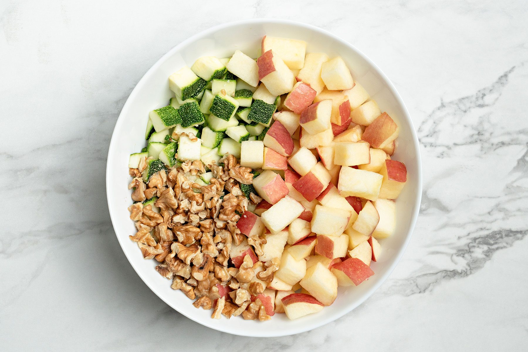 Apple Zucchini and walnuts combined in a large bowl.